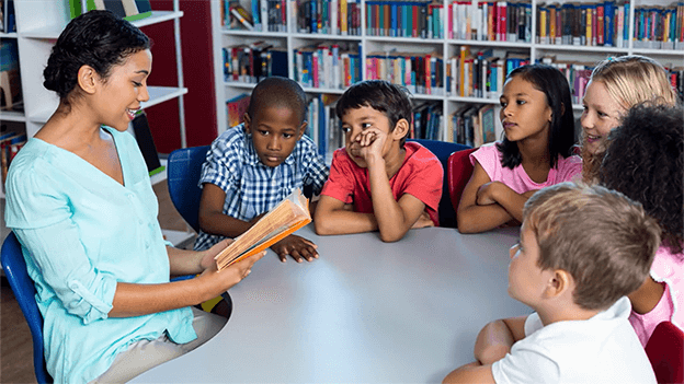 Enseignante en train de lire un livre à un groupe d’élèves dans la bibliothèque de l’école.